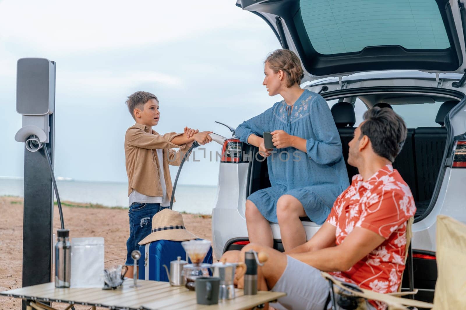 Family vacation trip traveling by the beach with electric car, happy family recharge EV car, enjoying outdoor camping coffee. Seascape travel and eco-friendly car for clean environment. Perpetual