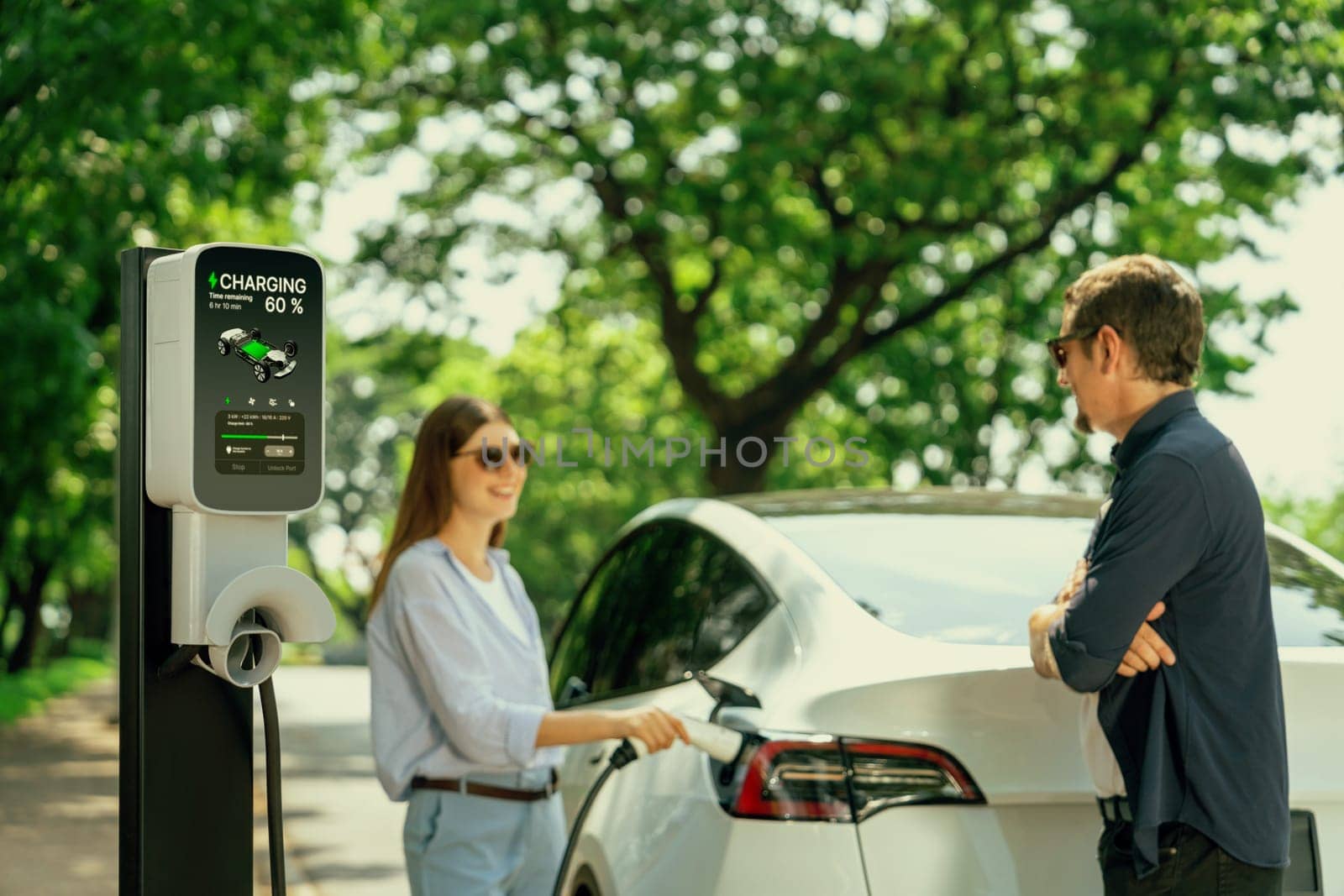 Lovely young couple recharging battery for electric car during road trip. Exalt by biancoblue