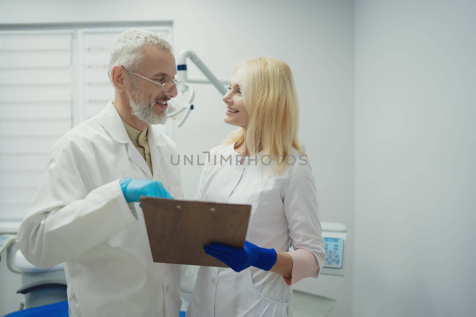 Male and female dental doctors wearing face sitting at his clinic. by Сookiestock