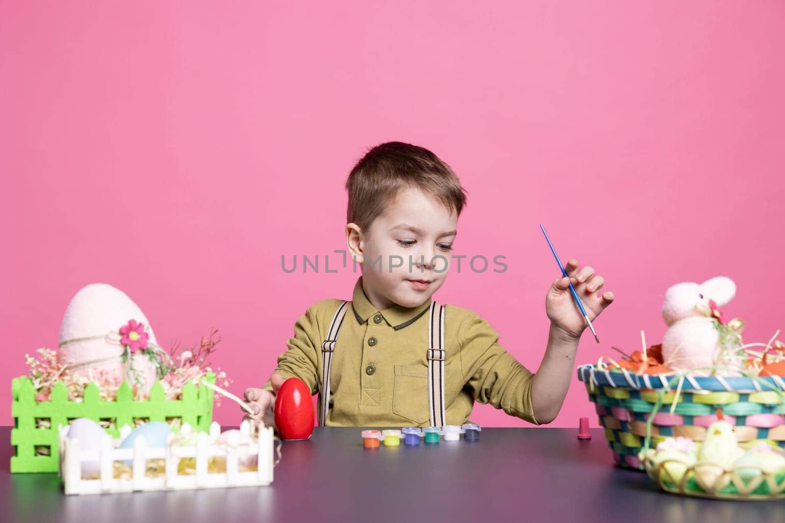 Lovely youngster with a smile crafting eggs and decorations for the Easter festivities, using art supplies and watercolor paint. Little pleased boy feeling excited about painting activity.