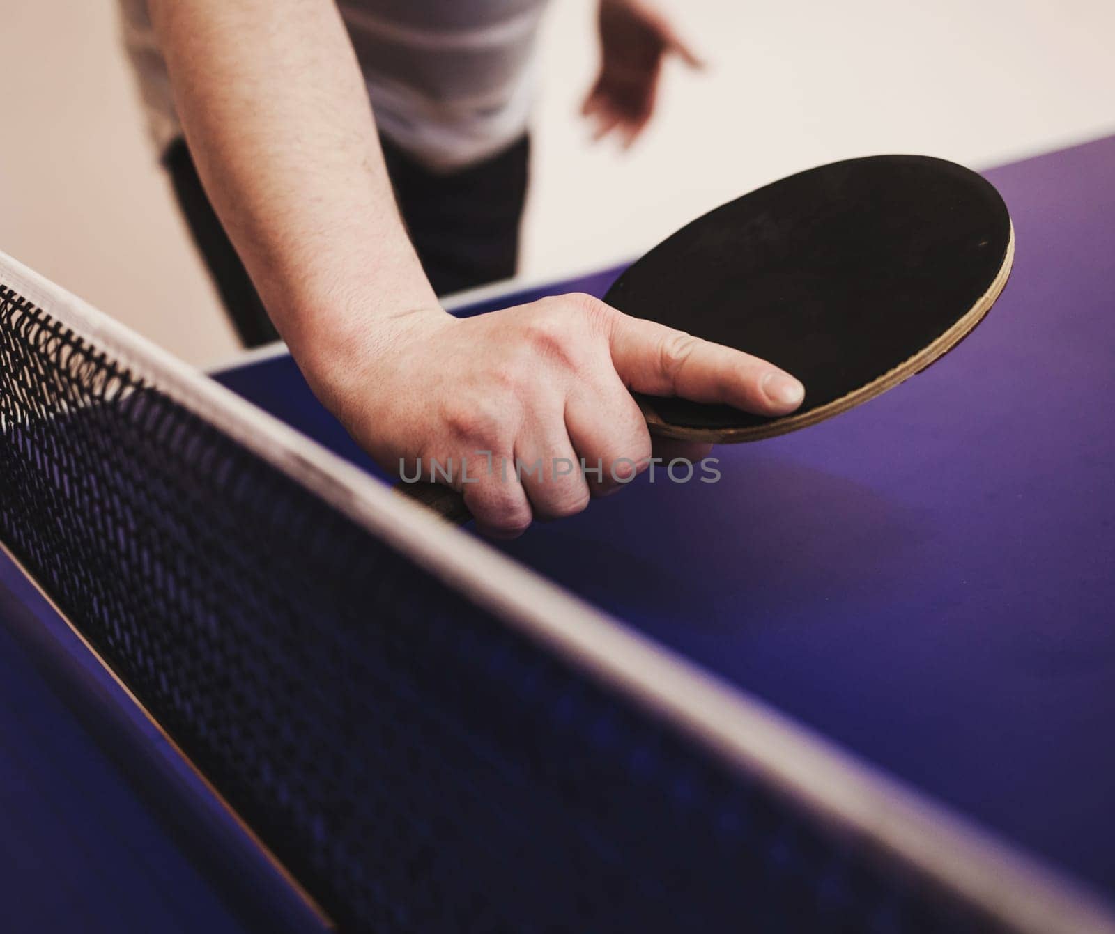 player's hand with a tennis racket on a blue table background. ping pong game