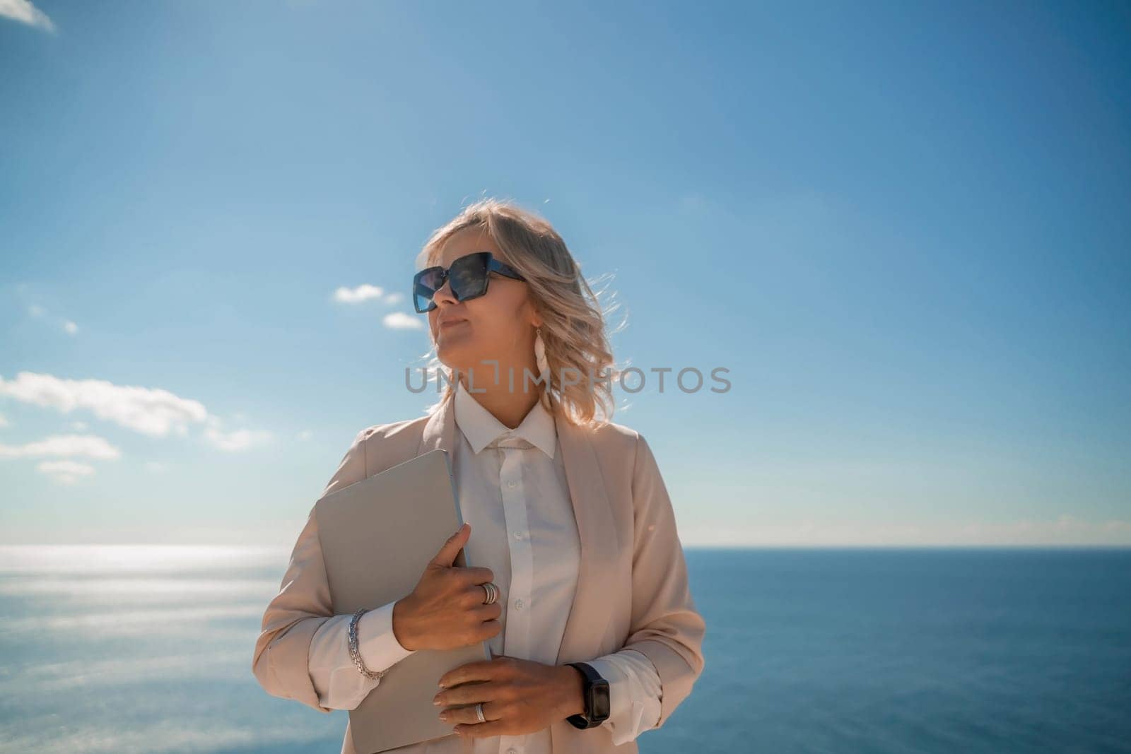 Freelance women sea working on a computer. Pretty middle aged woman with computer and phone outdoors with beautiful sea view. The concept of remote work