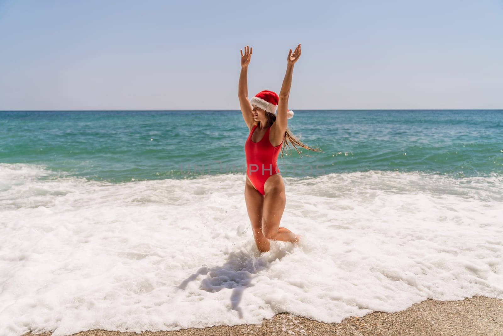 A woman in Santa hat on the seashore, dressed in a red swimsuit. New Year's celebration in a hot country