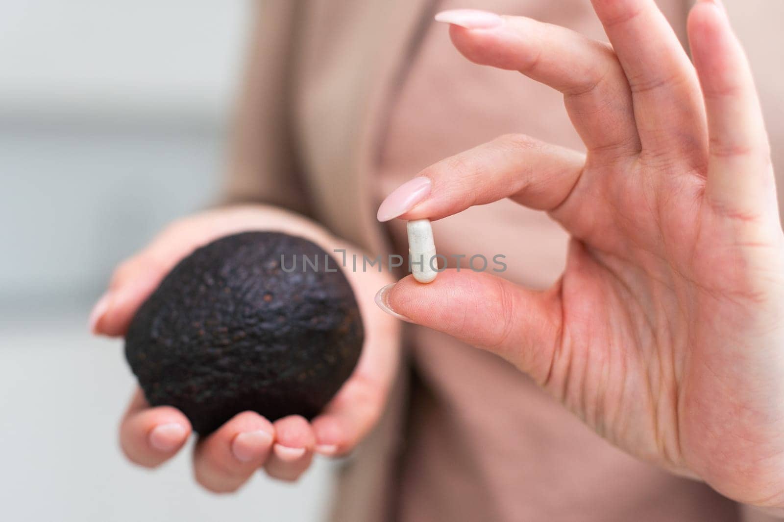 Young woman holds an avocado in one hand, vitamins capsules in the other. Choosing between healthy food and pills. Conceptual photo on white background. High quality photo