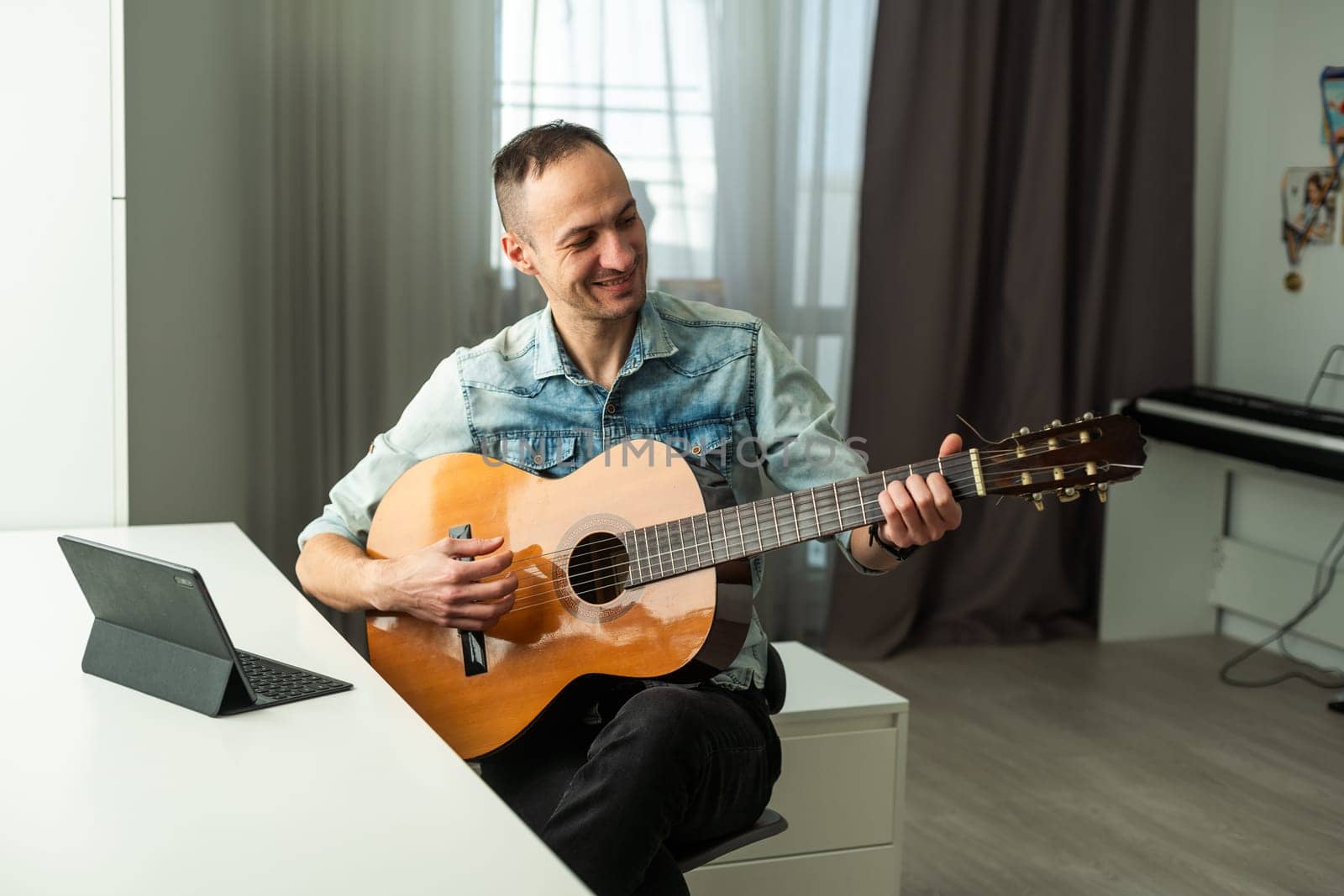 Caucasian man remotely teaches guitar playing on the laptop. Online music training. High quality photo