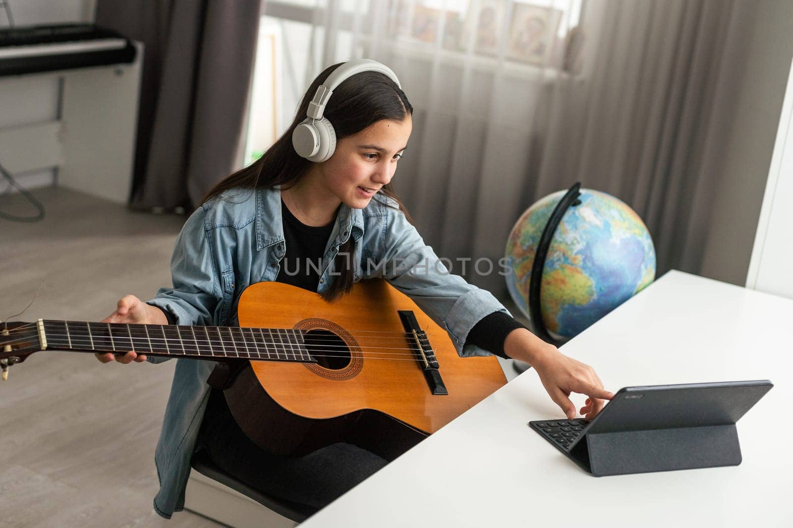 Teenager girl learning to play guitar at home using online lessons. Hobby remote musical education acoustic guitar. Copy space. High quality photo