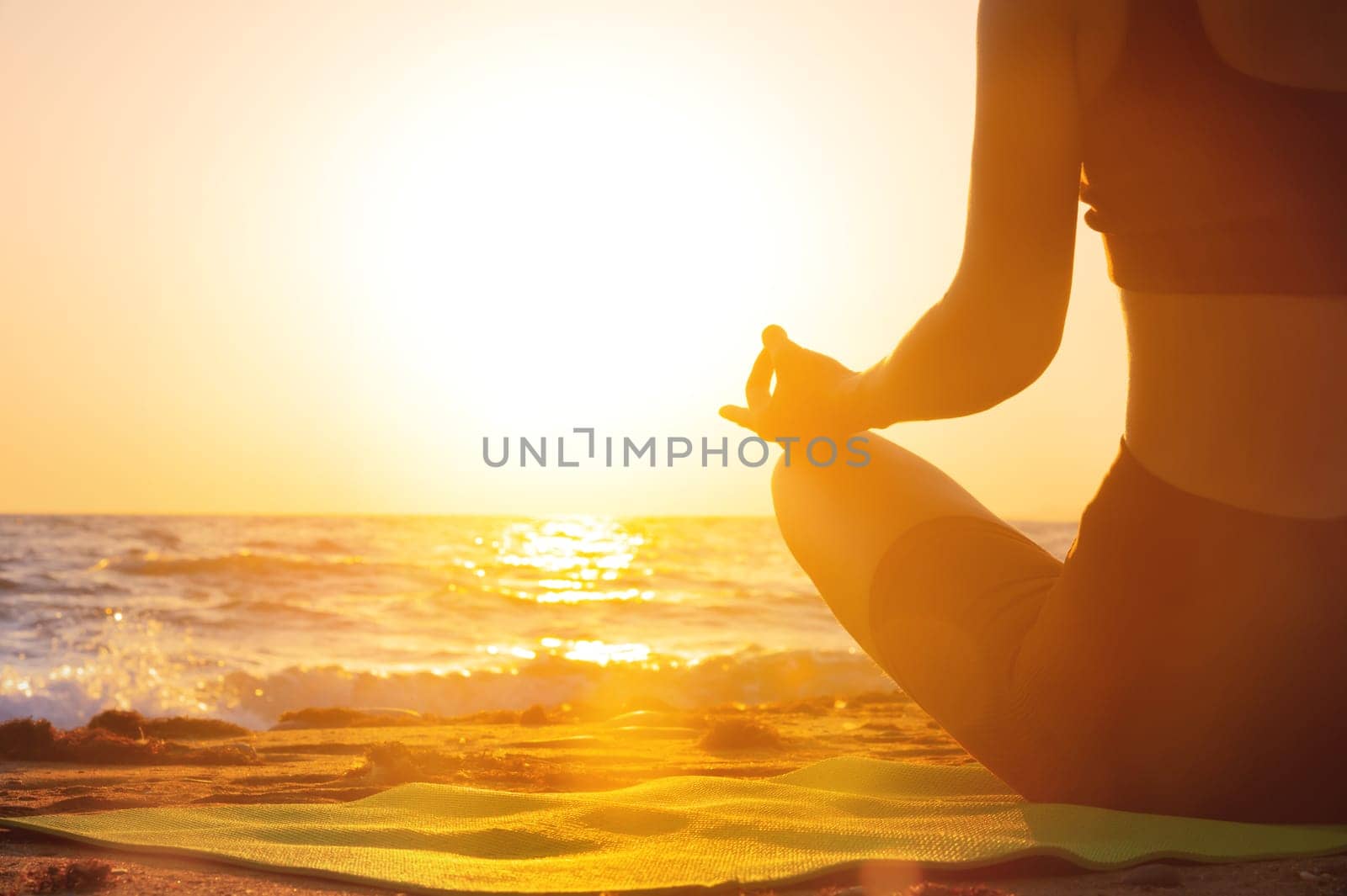Close-up Yoga woman meditating at serene sunset or sunrise on the beach. The girl relaxes in the lotus position. Fingers folded in mudras. by yanik88