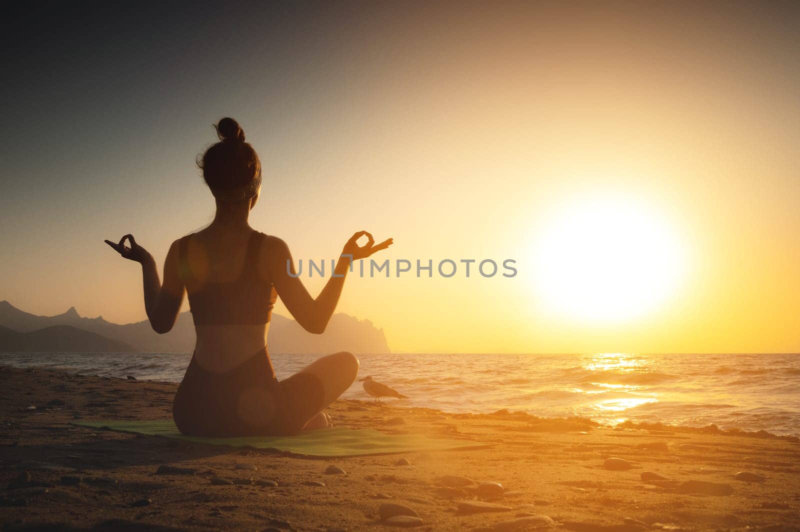 Yoga woman meditating at serene sunset or sunrise on the beach. The girl relaxes in the lotus position. Fingers folded in mudras