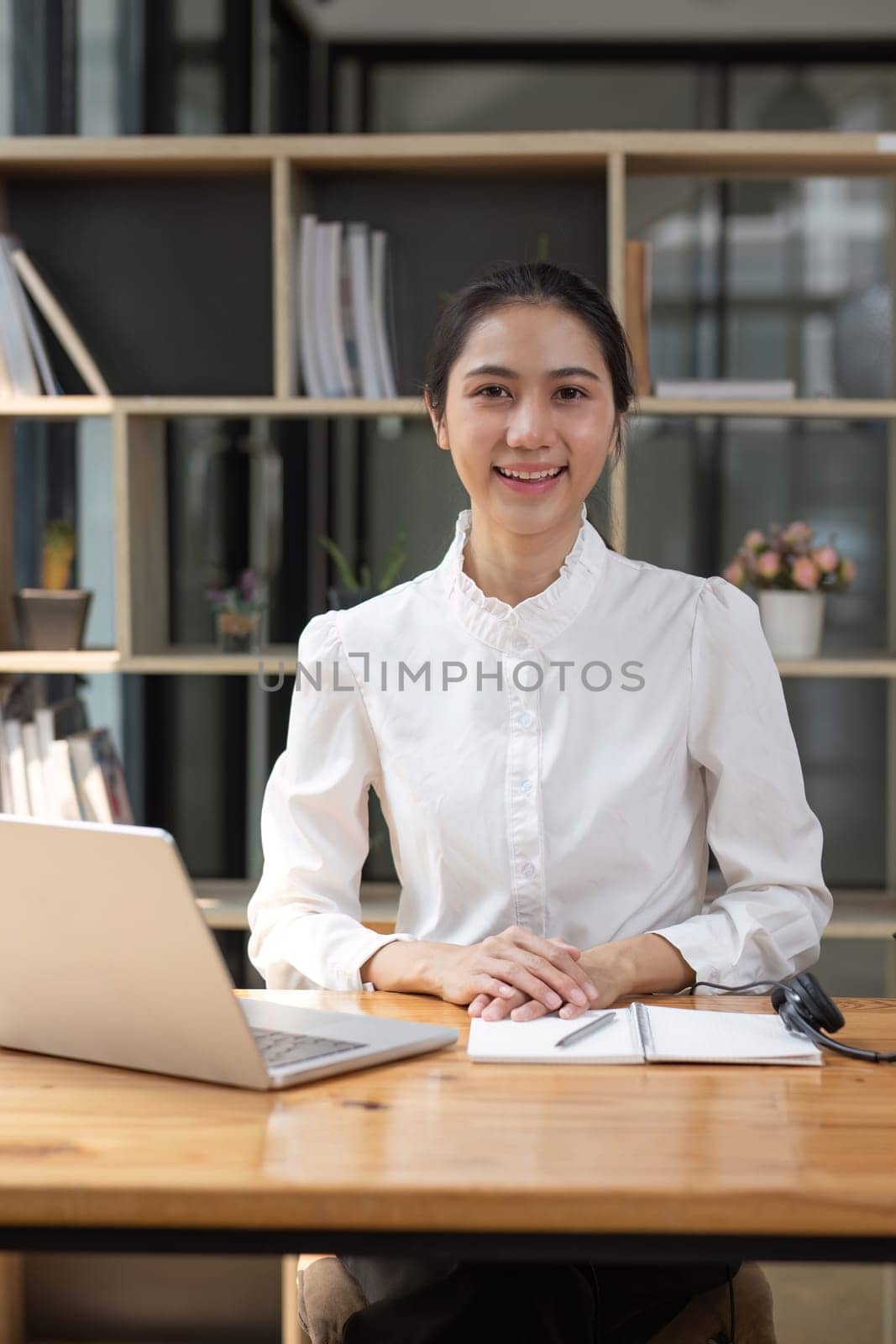 Portrait of smiling Asian businesswoman working on laptop on wooden table in office room. by wichayada