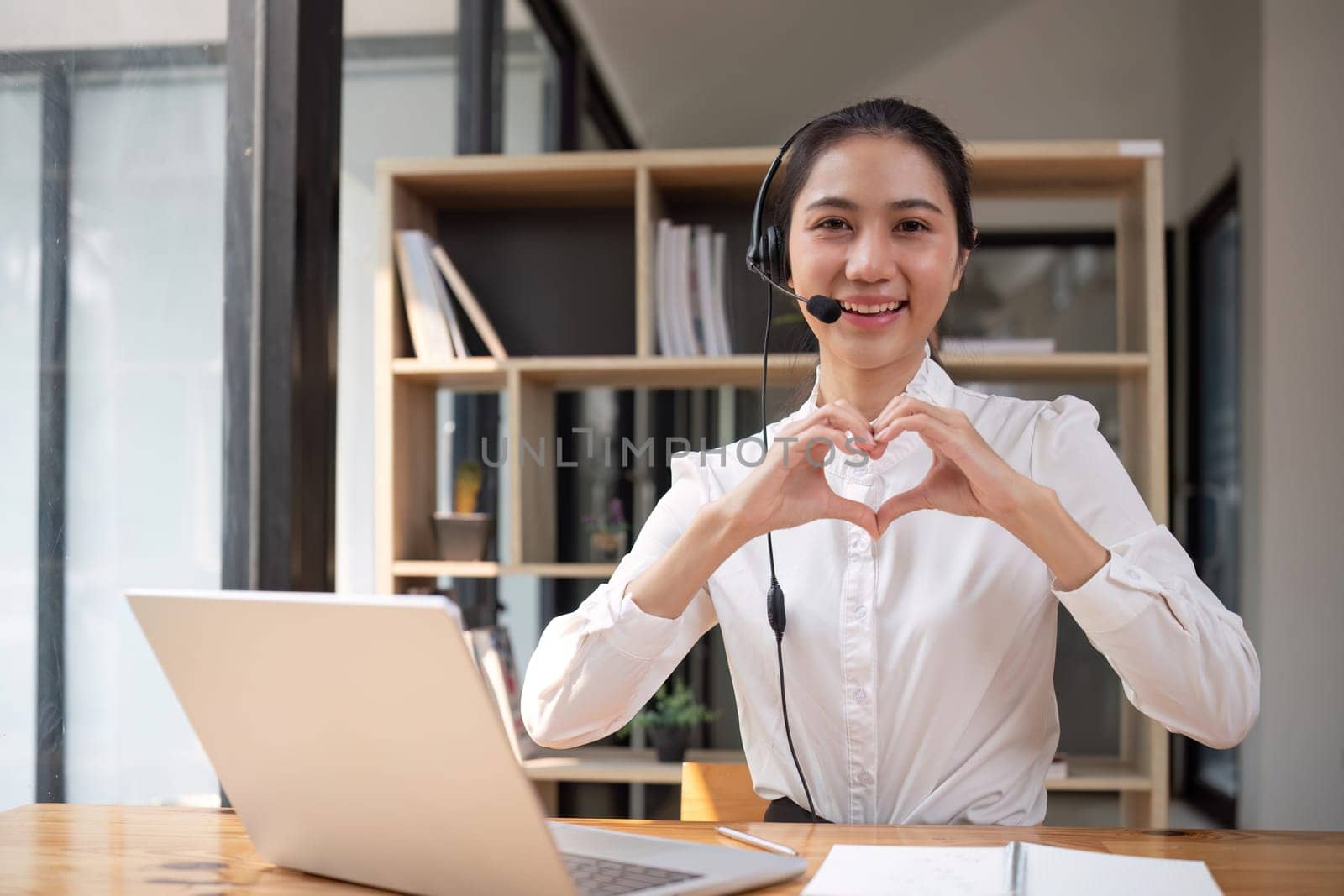 Call center operator makes heart-shaped hand gesture Wear headphones to talk to customers. Provide consultation via online channels on laptops.