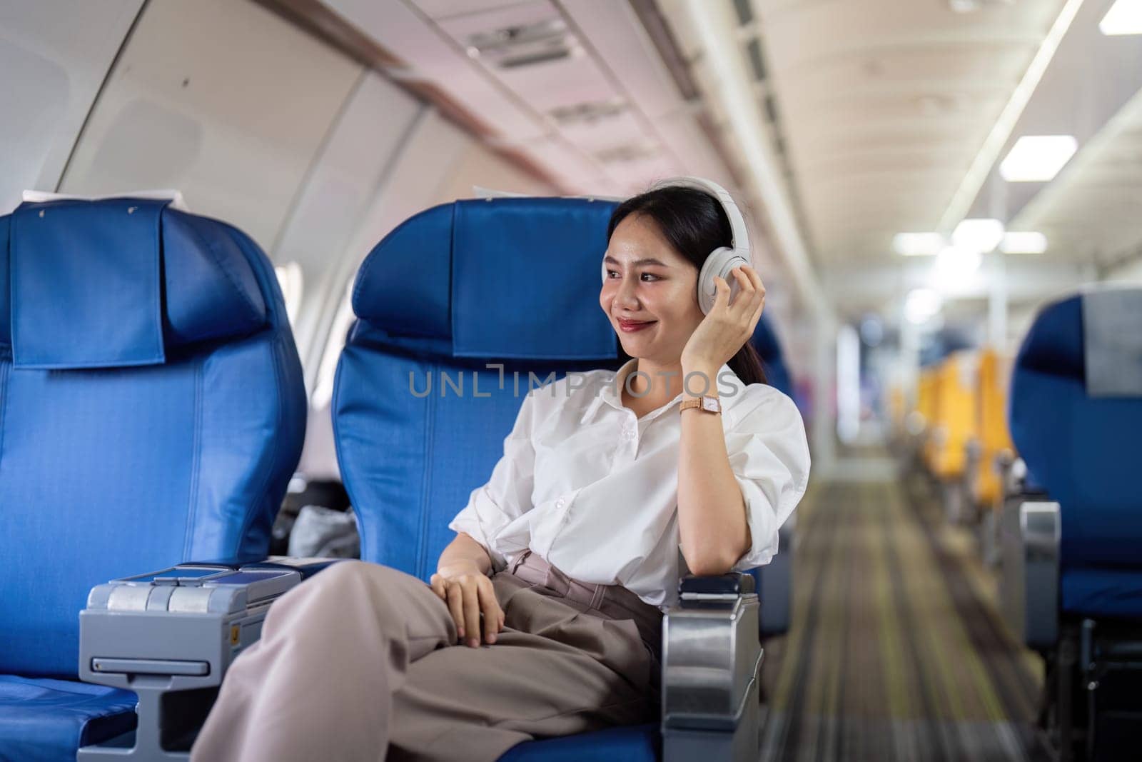 Asian young woman wearing headphone listen to music at first class on airplane during flight, Traveling and Business concept.