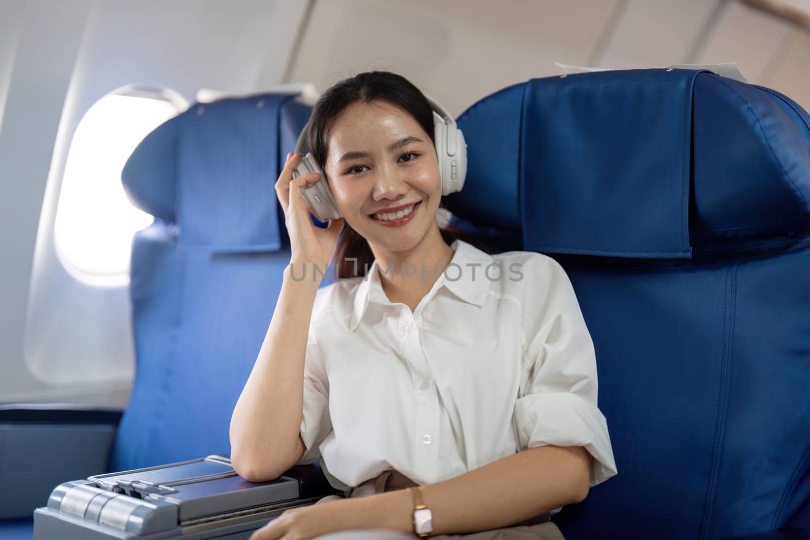 Asian young woman wearing headphone listen to music at first class on airplane during flight, Traveling and Business concept by nateemee