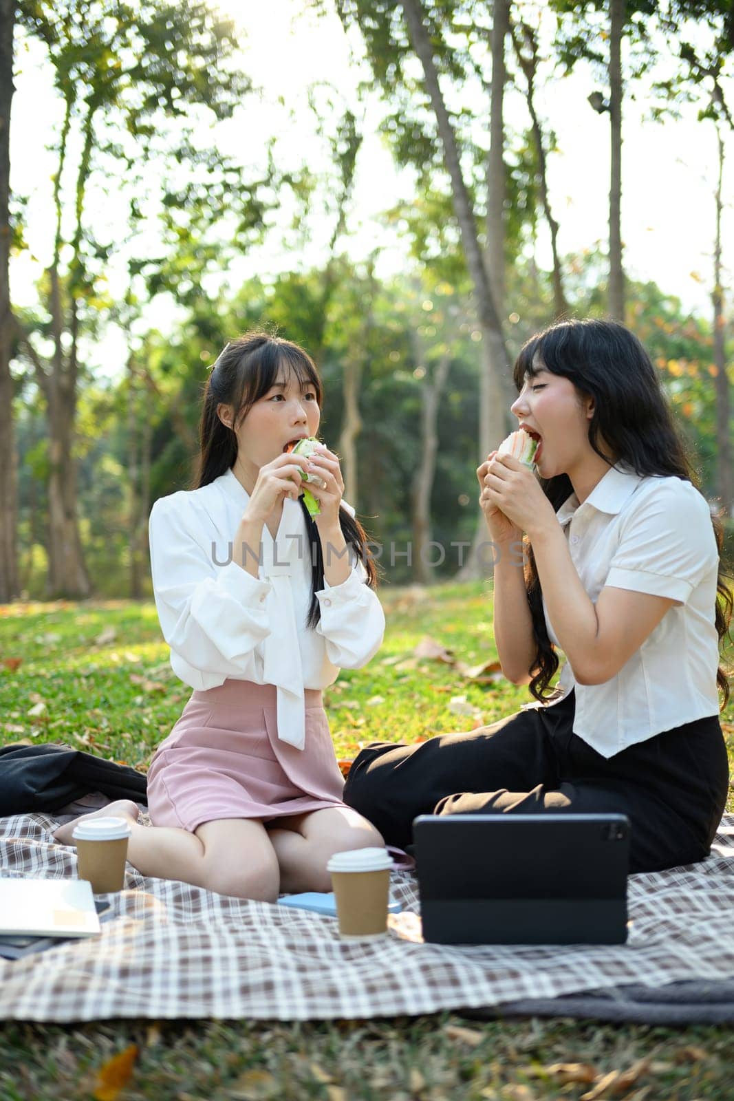 Cheerful female colleagues enjoying sandwich during lunch break at outdoor by prathanchorruangsak