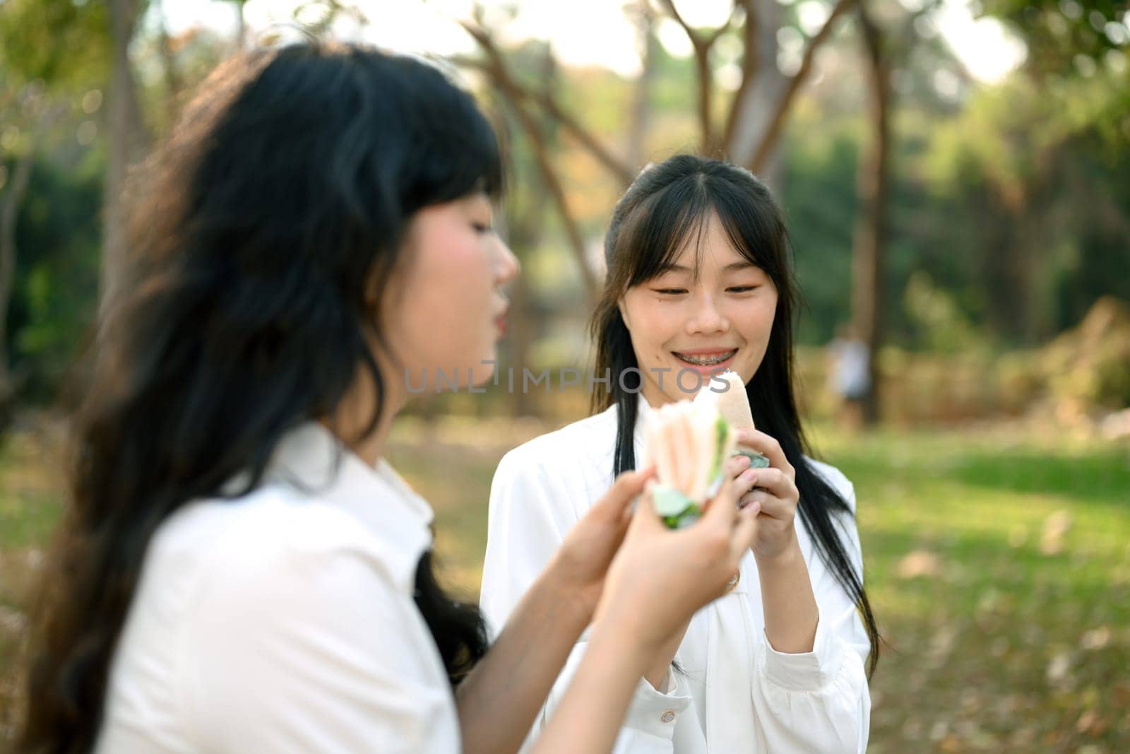 Cheerful female colleagues enjoying sandwich during lunch break at outdoor by prathanchorruangsak