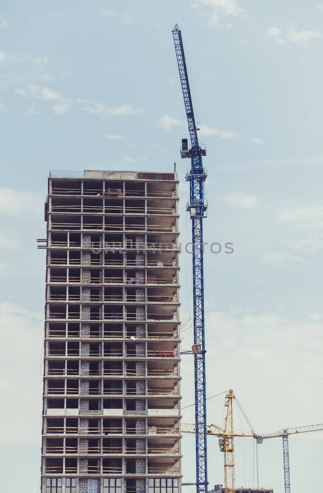 three building cranes at the background of a multi-storey building under construction. New houses will wait for families