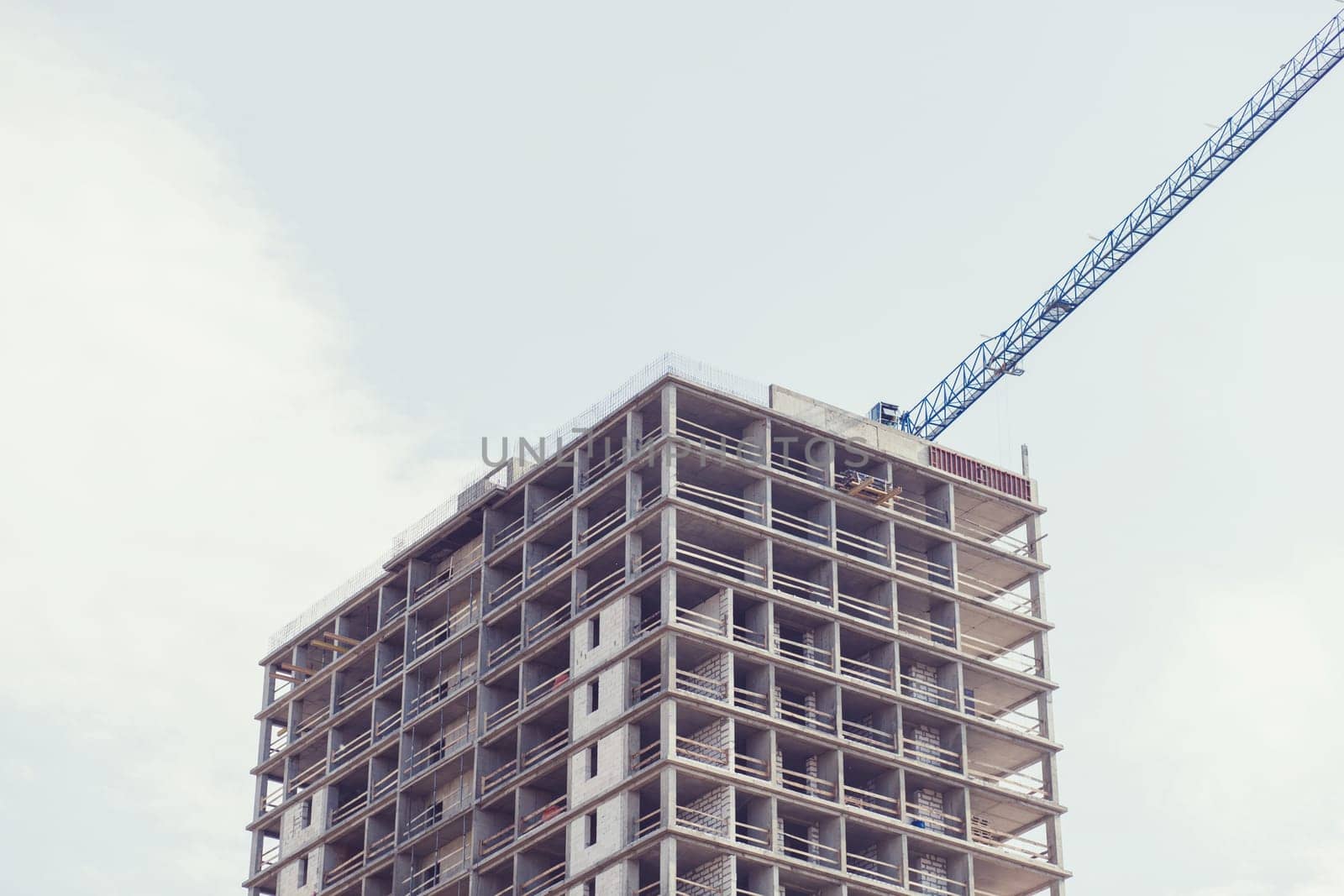 fragment of unfinished building with cranes against the blue sky
