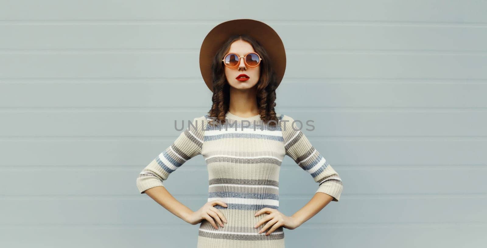 Stylish young woman posing in round hat, knitted dress, sunglasses in the city