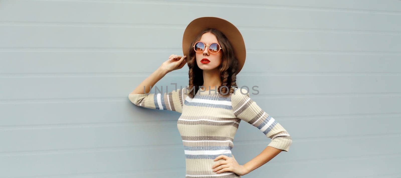 Stylish young woman posing in round hat, knitted dress, sunglasses in the city