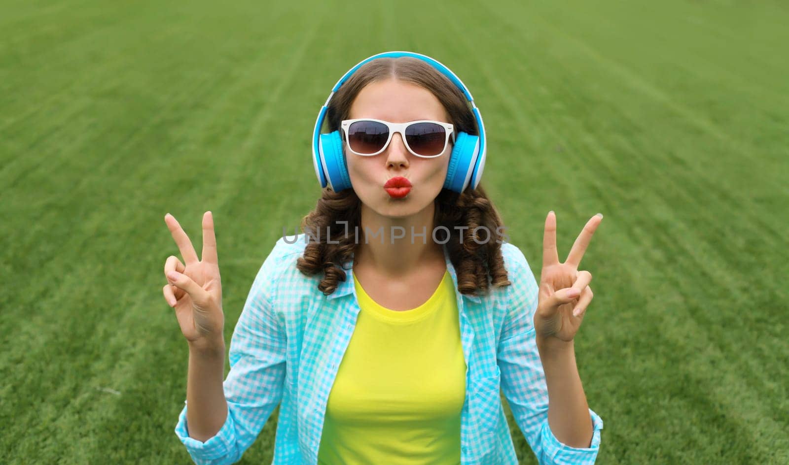 Portrait of happy smiling young woman listening to music in headphones while lying on grass in summer park