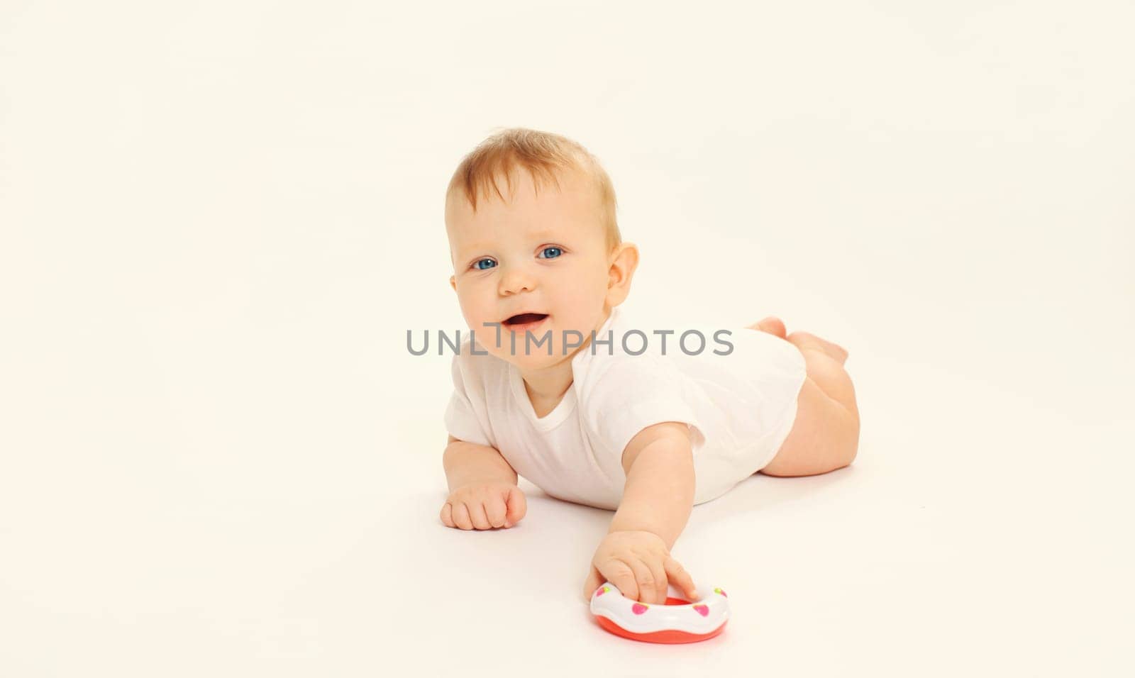 Happy little baby playing with toys while sitting on floor on white studio background