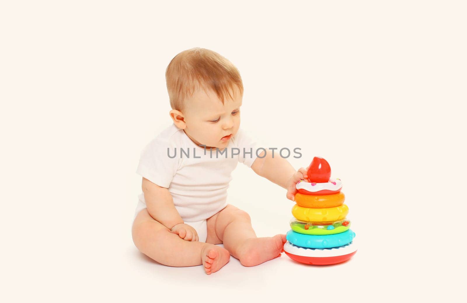 Happy little baby playing with toys while sitting on floor on white studio background