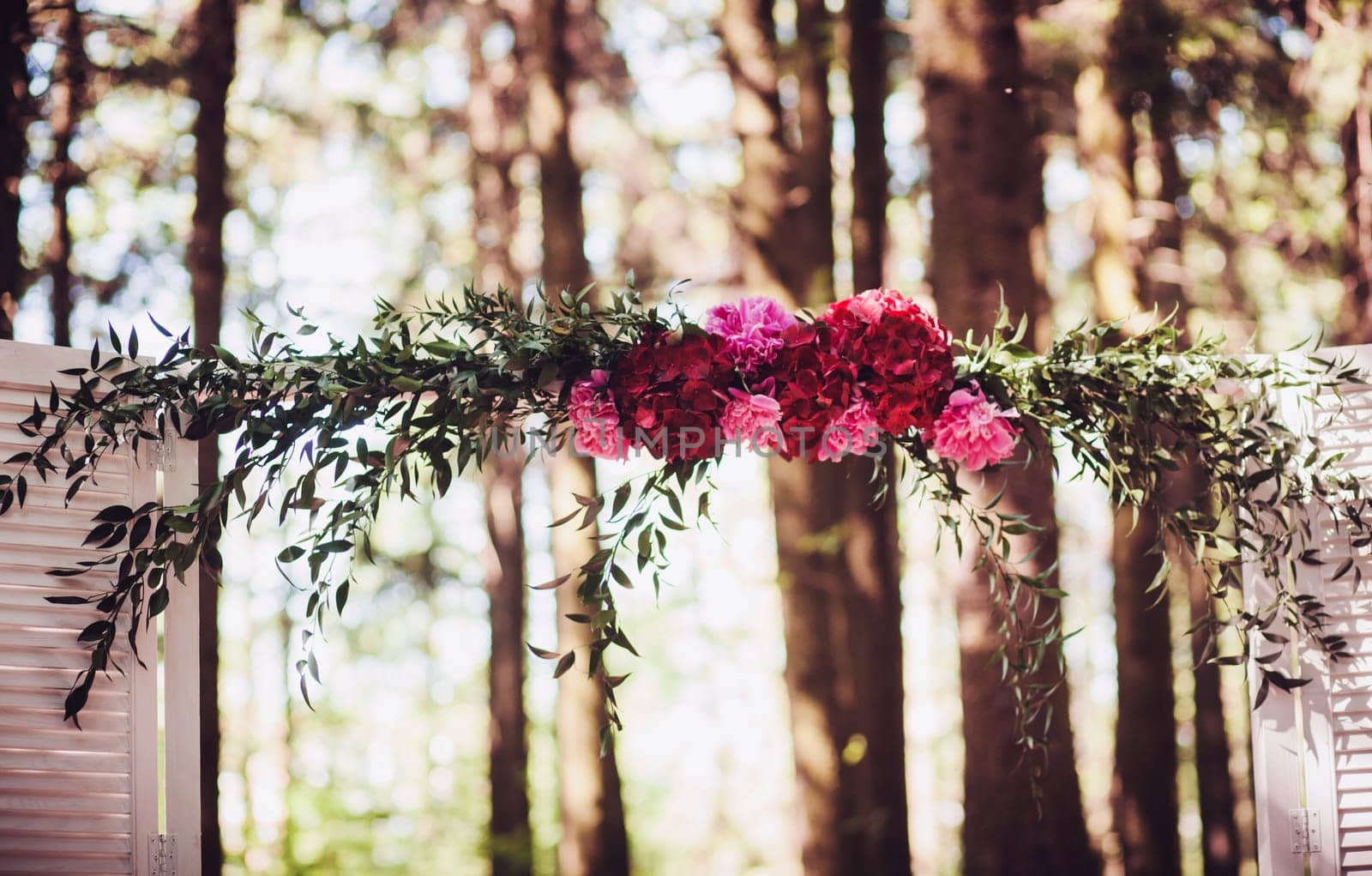 Beautiful white wedding arch decorated with bright flowers outdoors
