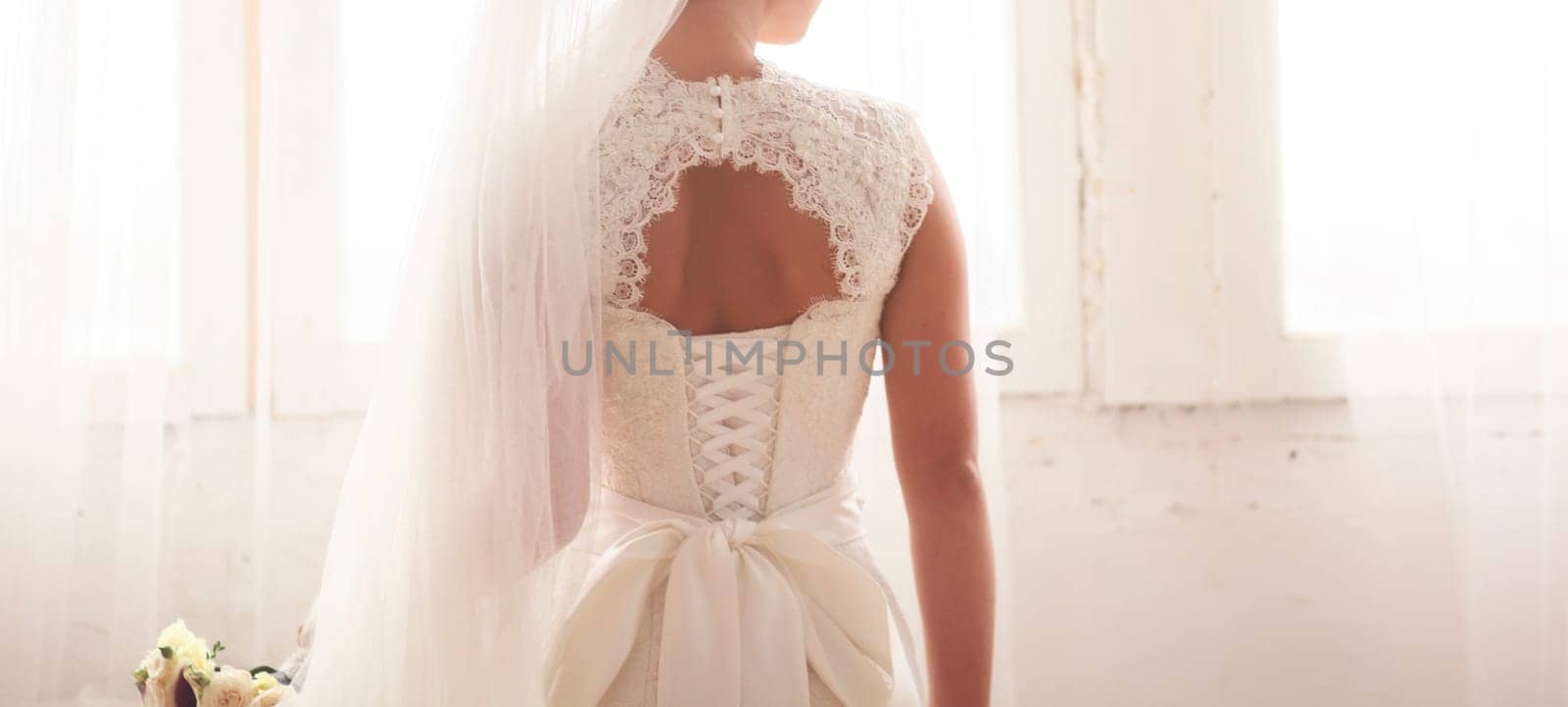 Beautiful bride on room background. On the woman in wedding dress with lace and an open back