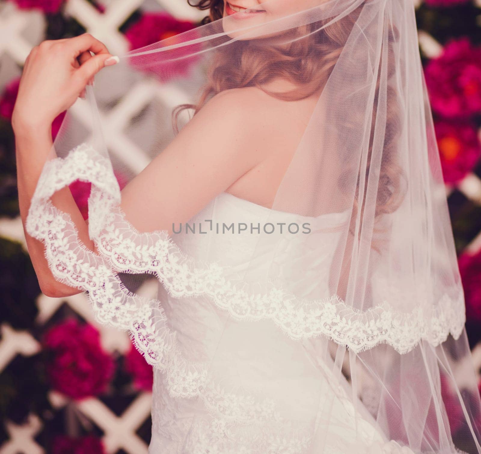 Portrait of young beautiful happy bride in white lace wedding dress holding veil