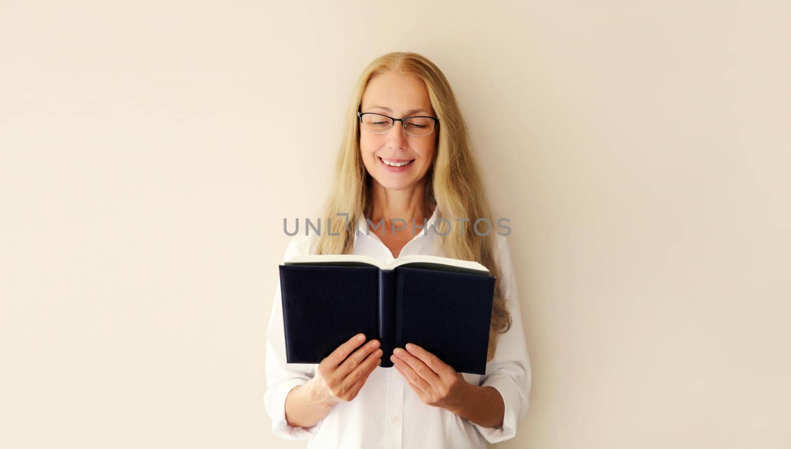 Portrait of happy caucasian middle-aged woman reading book with blank cover on white studio background