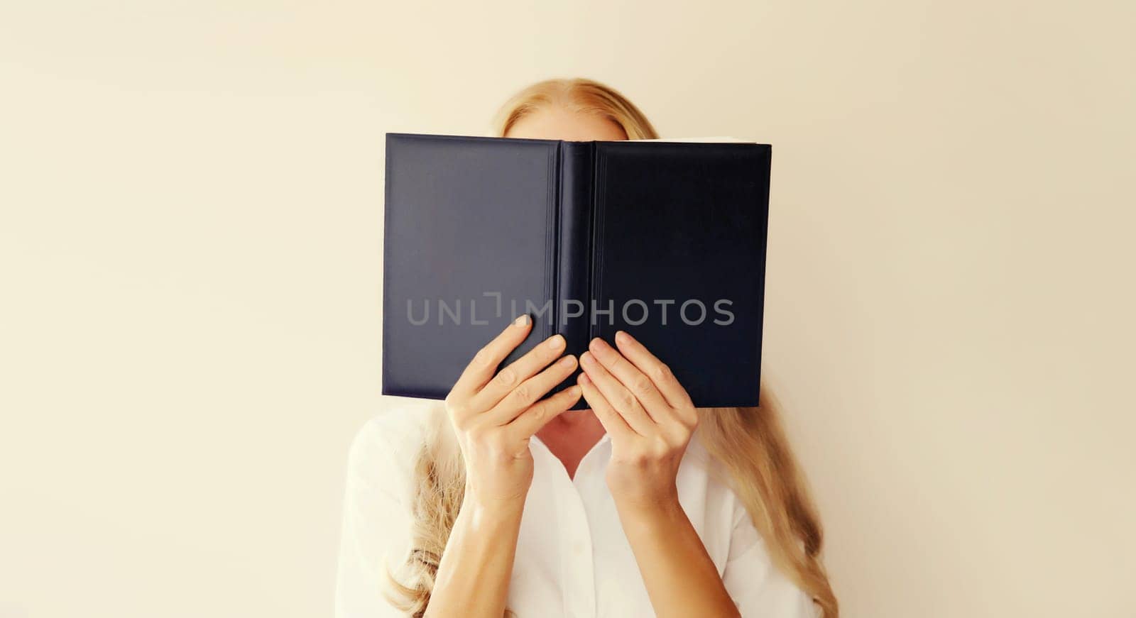 Young sad tired woman student covering her face with open book with blank cover on white background