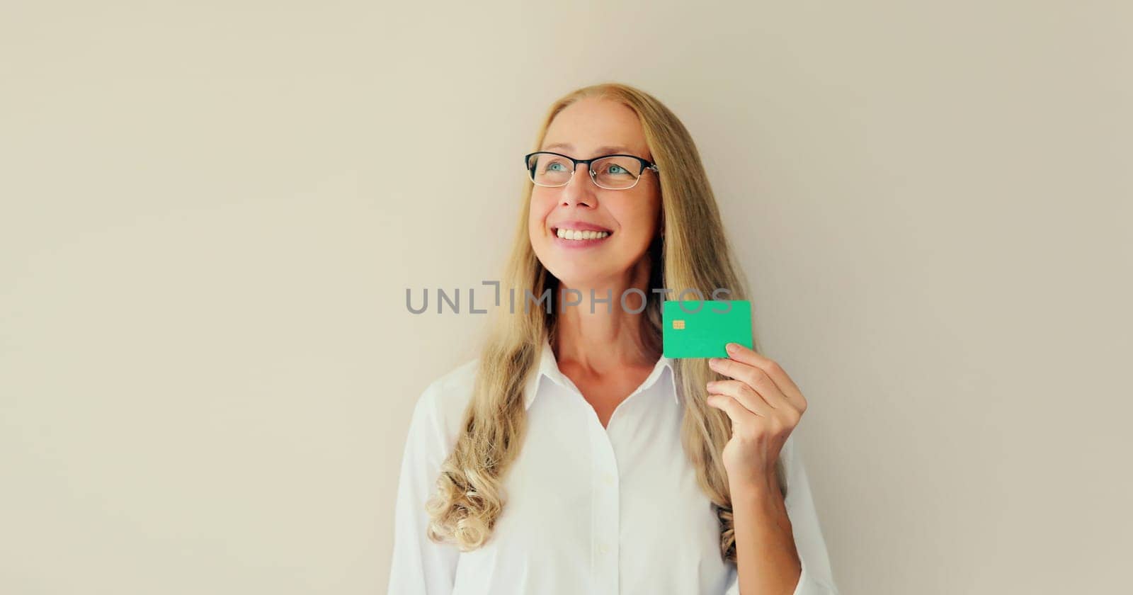 Portrait of happy successful smiling middle-aged woman holding plastic credit bank card on studio white background