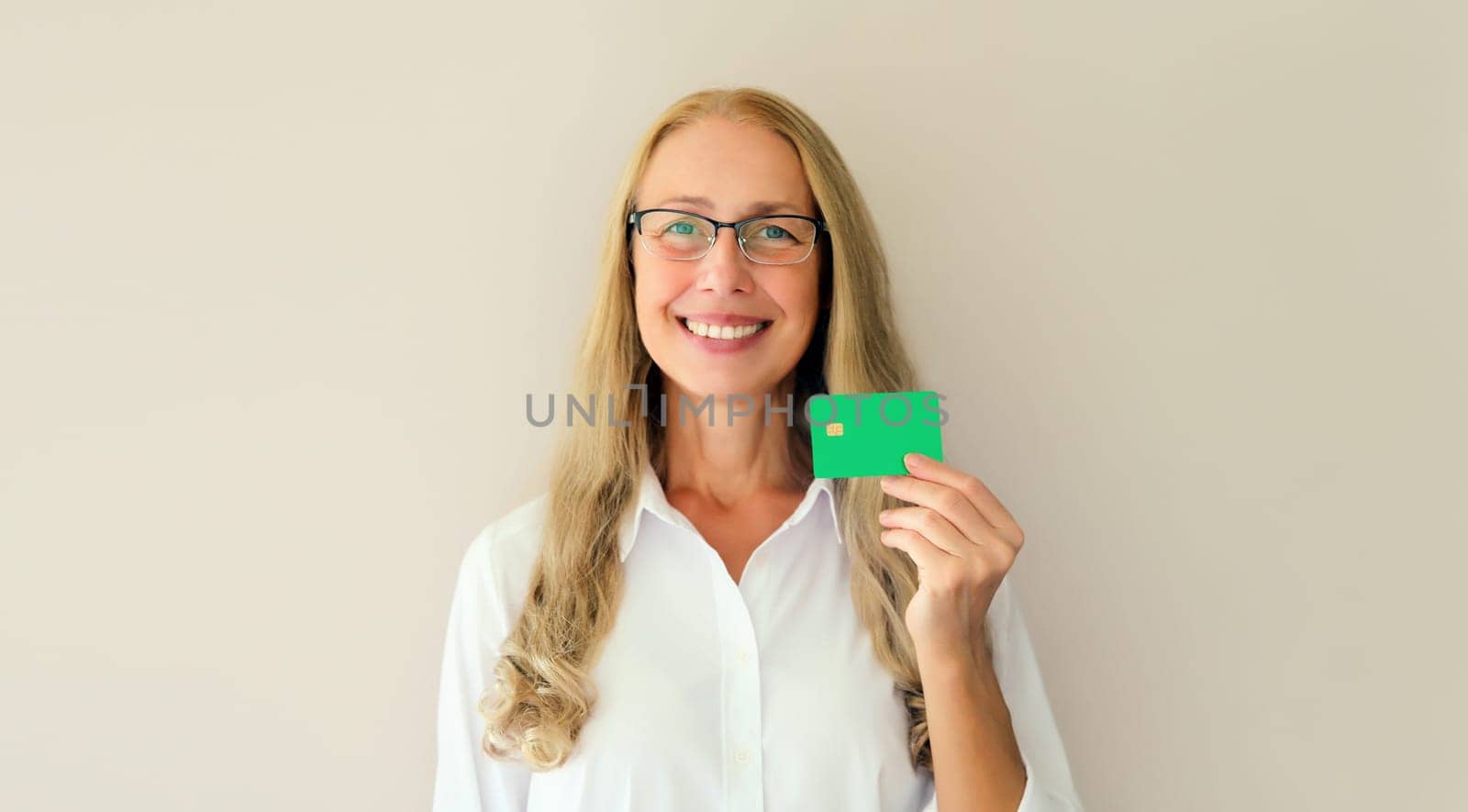 Portrait of happy successful smiling middle-aged woman holding plastic credit bank card on studio white background