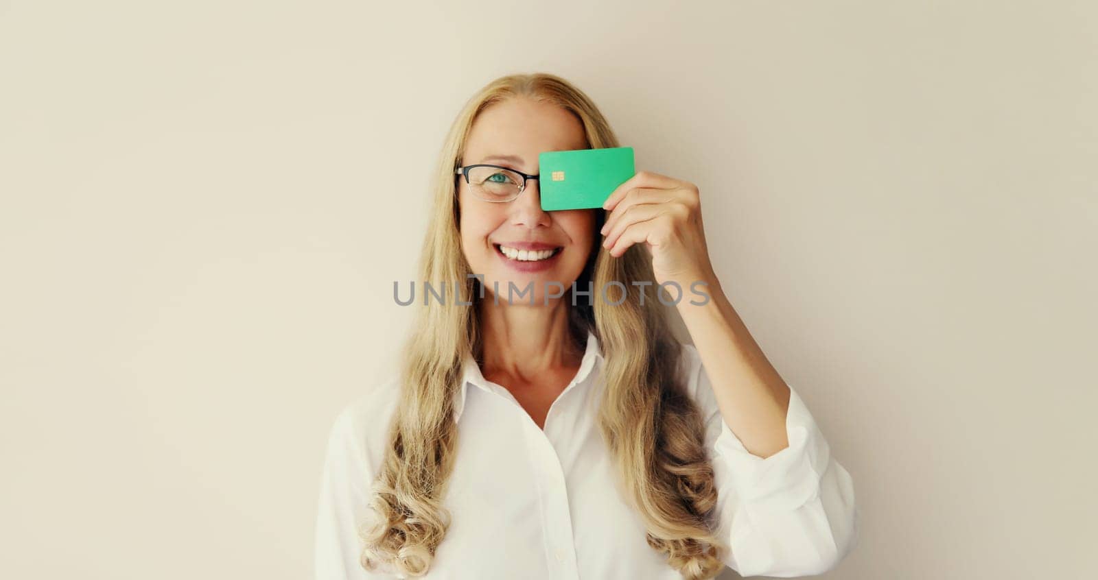 Portrait of happy successful smiling middle-aged woman holding plastic credit bank card on studio white background