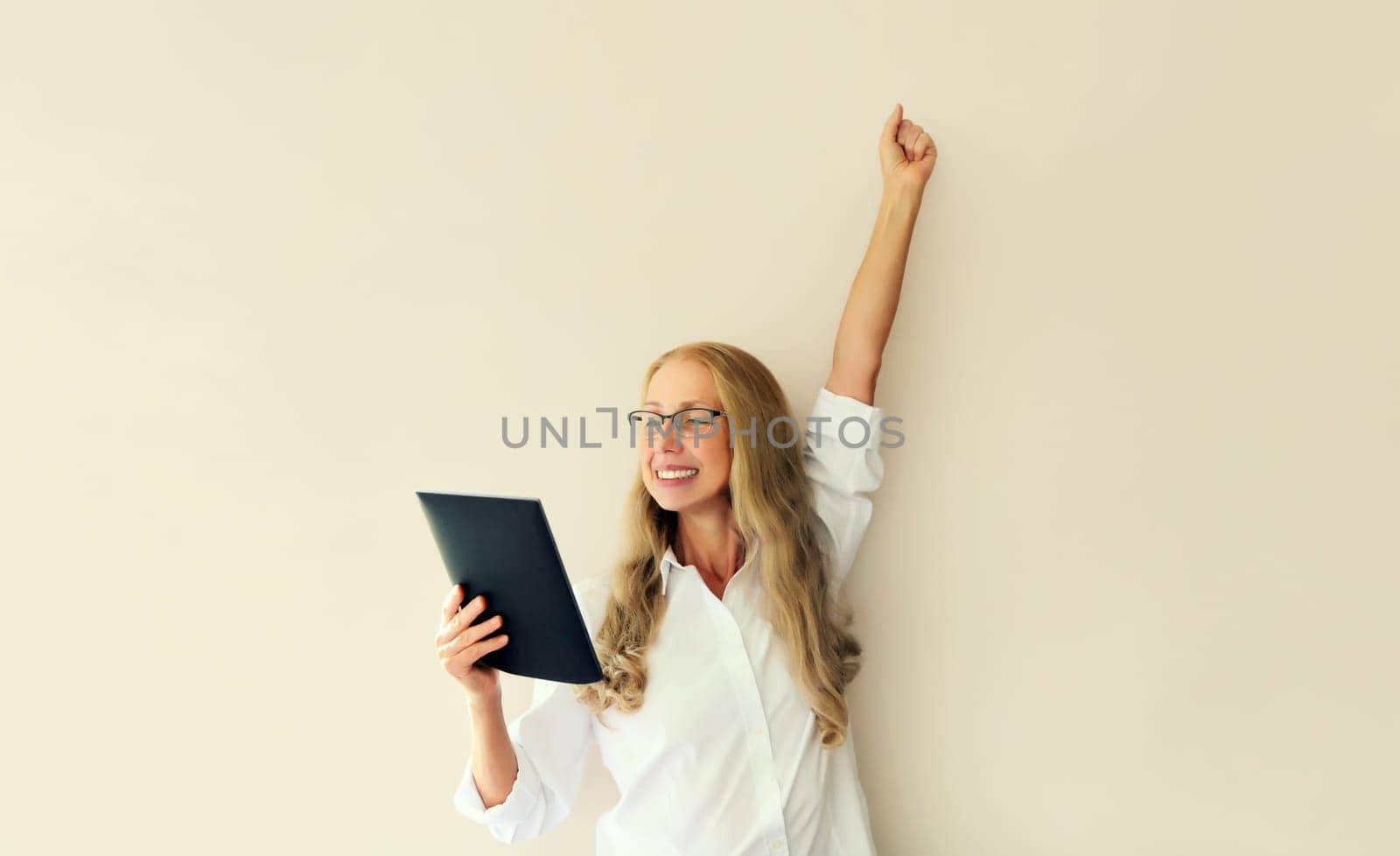 Happy joyful middle-aged woman employee looking at digital tablet computer celebrating victory, feeling success on white studio background