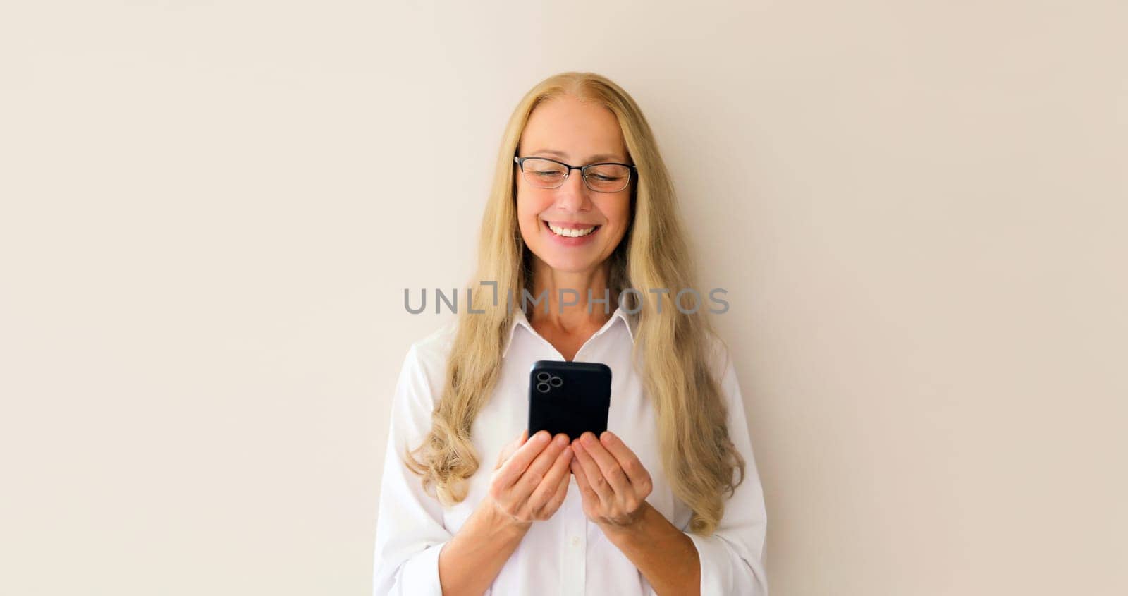 Portrait of happy smiling middle-aged woman with mobile phone looking at device on white studio background
