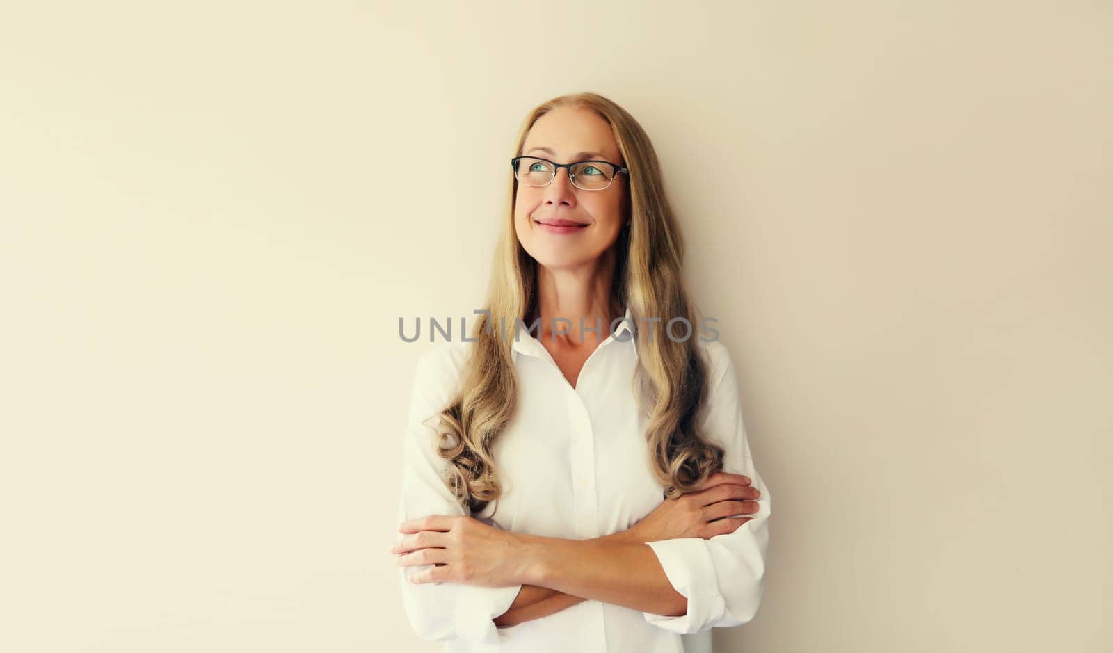 Portrait of happy smiling caucasian middle aged woman employee manager looking away in eyeglasses with crossed arms on white studio background