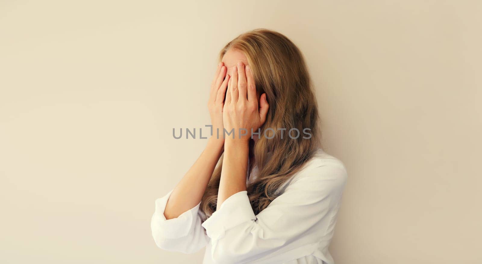 Upset sad crying woman covering her eyes and face with hands while experiencing mental or physical suffering on studio background