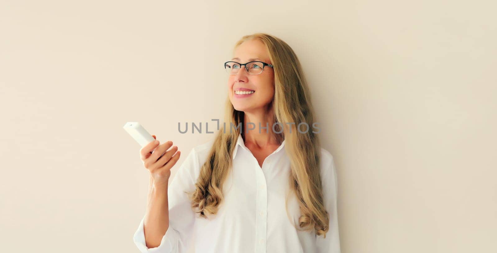 Portrait of happy smiling caucasian middle-aged woman turns on the air conditioner or TV using the remote control at home