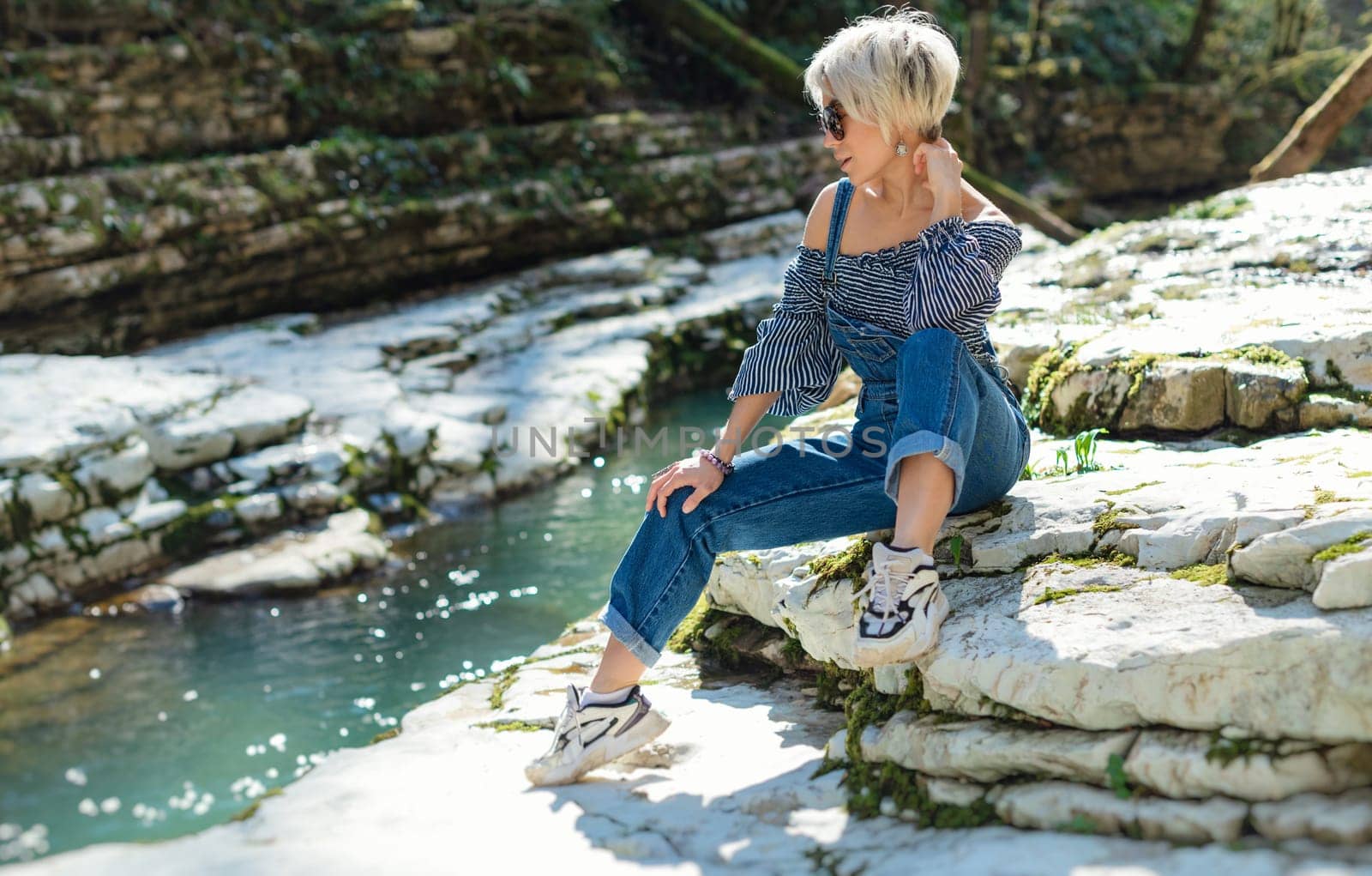 beautiful sexy girl in nature among a mountain river and a rocky canyon in a denim jumpsuit smiles cheerfully and enjoys life on vacation in the summer