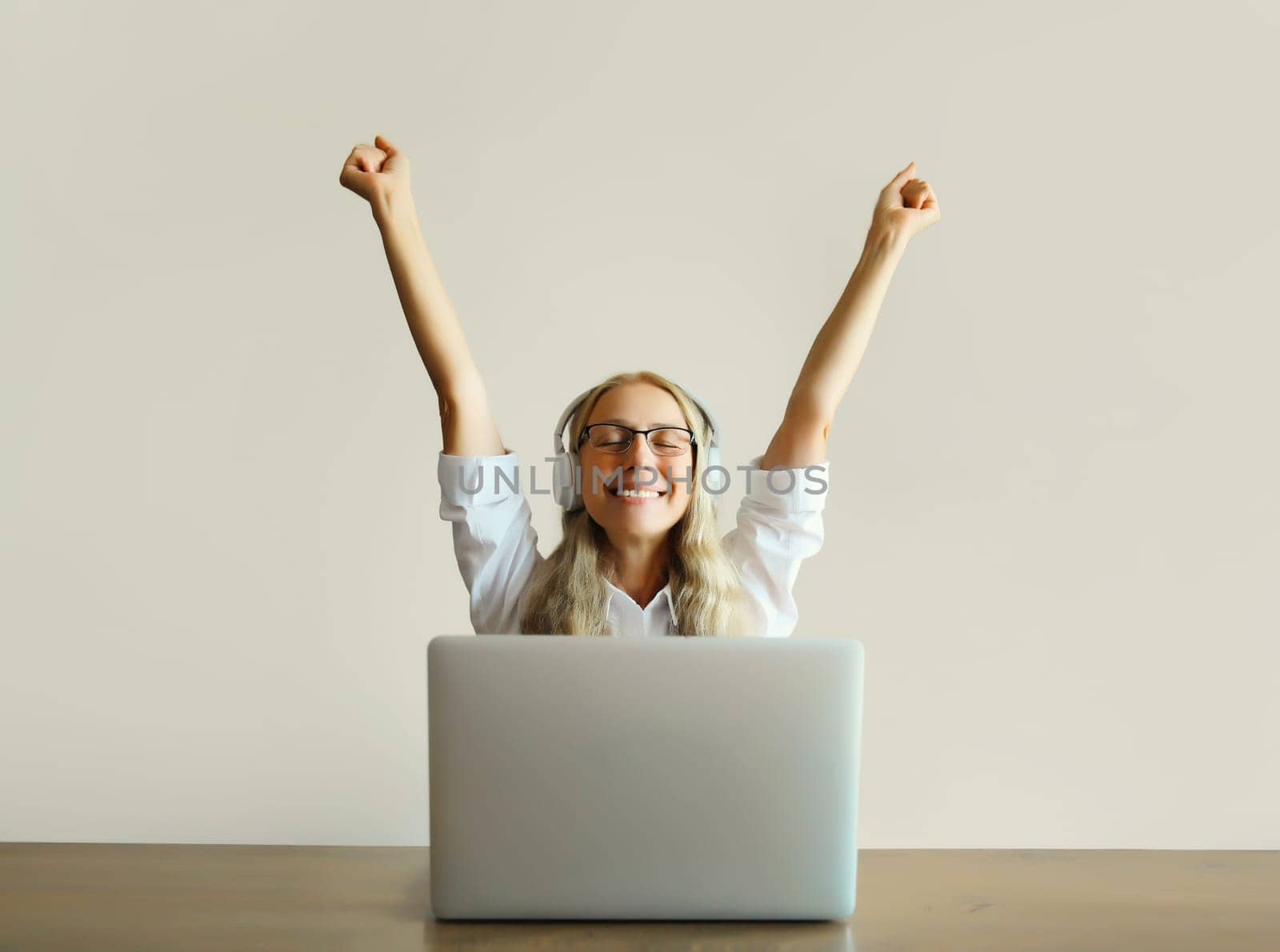 Happy joyful middle aged woman listening to music in headphones working with laptop computer sitting at desk at home