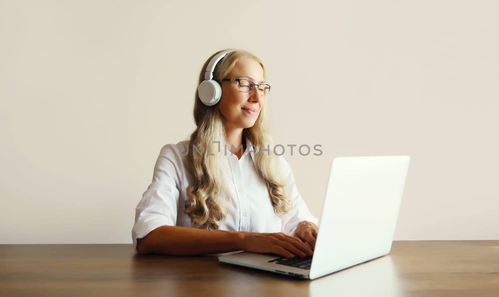 Happy relaxing middle aged woman listening to music in headphones working with laptop computer sitting at desk at home