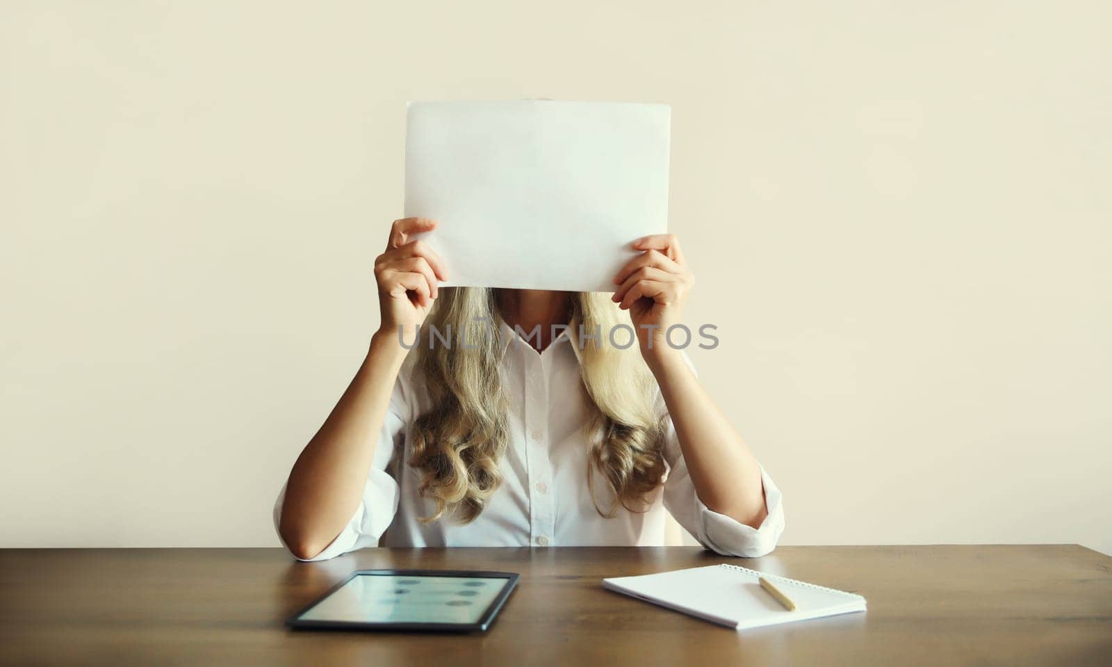 Woman showing and holding white blank sheet of paper document for text copy space while working with digital tablet computer sitting at the desk