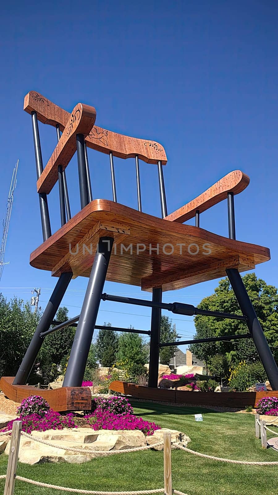 Whimsical oversized wooden chair sculpture in a beautiful public garden under clear blue sky