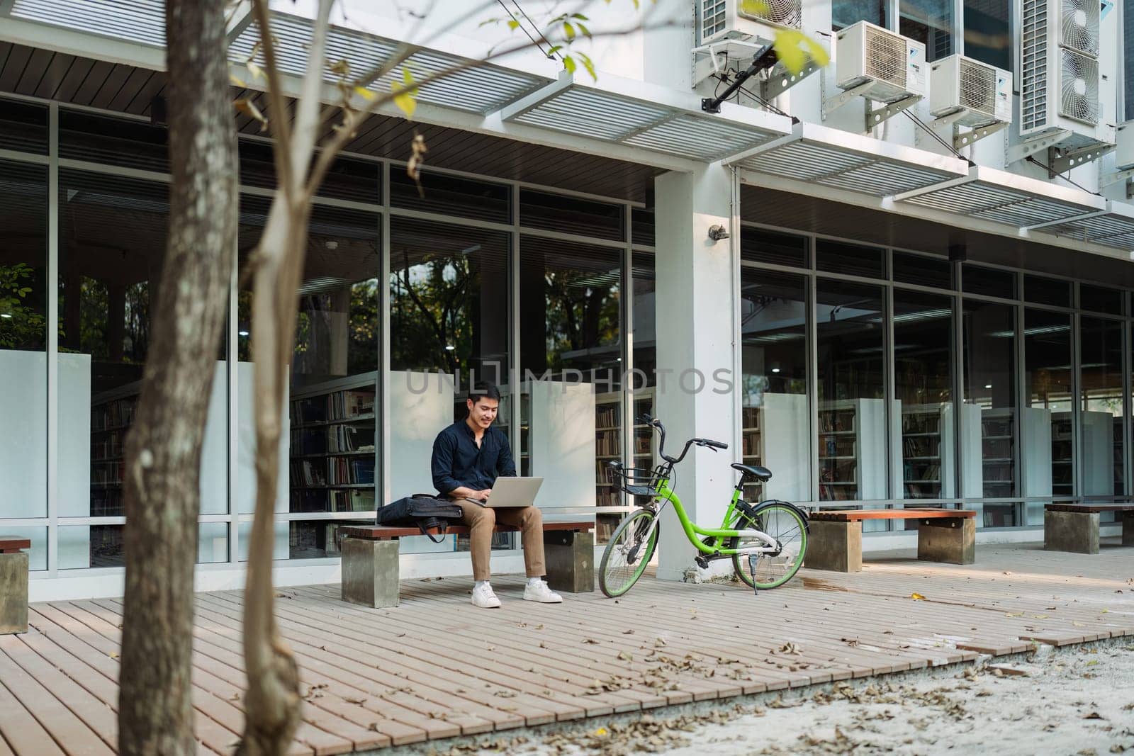 business man sitting on bench and working remotely on project with laptop by itchaznong