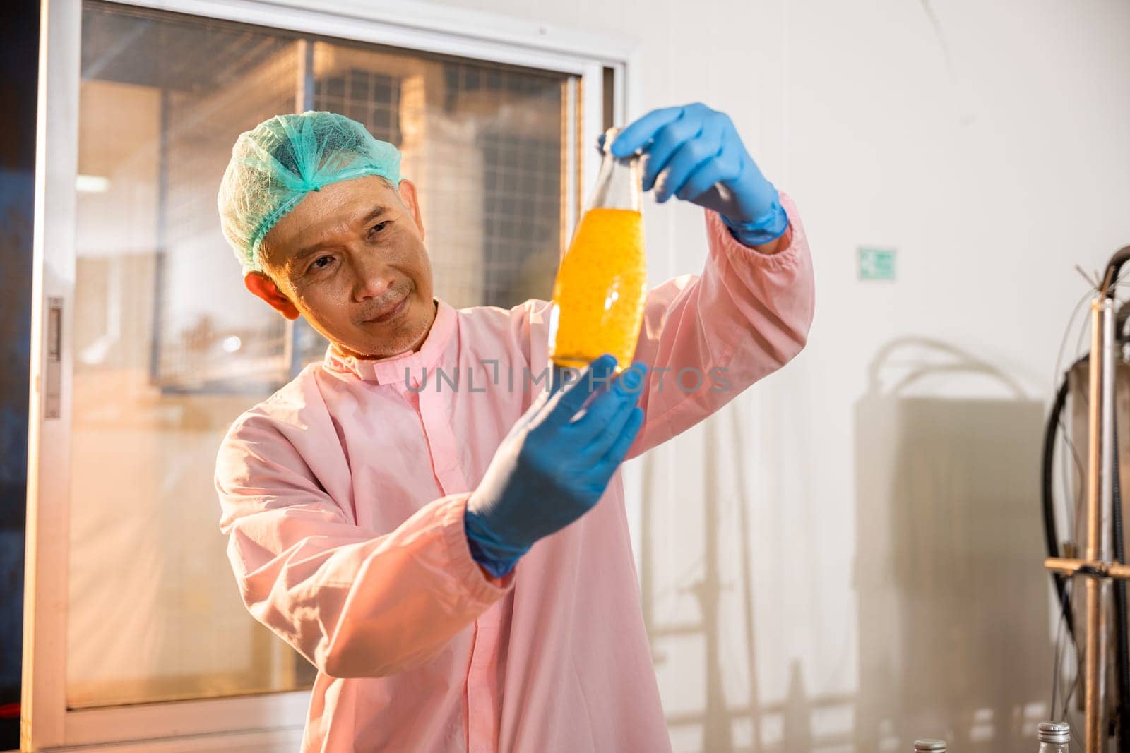 A male worker dressed in a uniform and gloves inspects Basil seed products on the conveyor belt by Sorapop