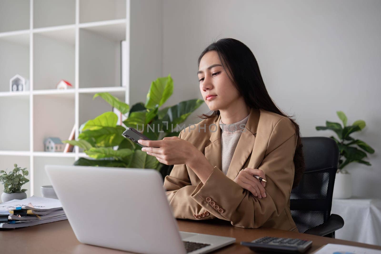 Unhappy Asian business woman shows stress over unsuccessful business while working in home office decorated with soothing green plants..