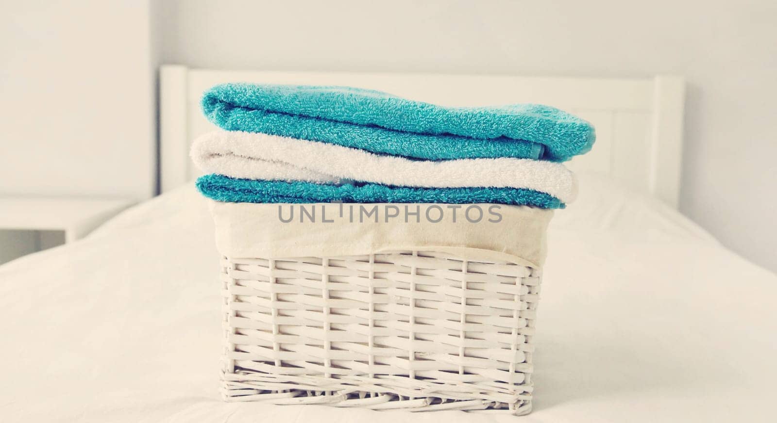 Wicker laundry basket with clean folded towels on the bed by Rohappy