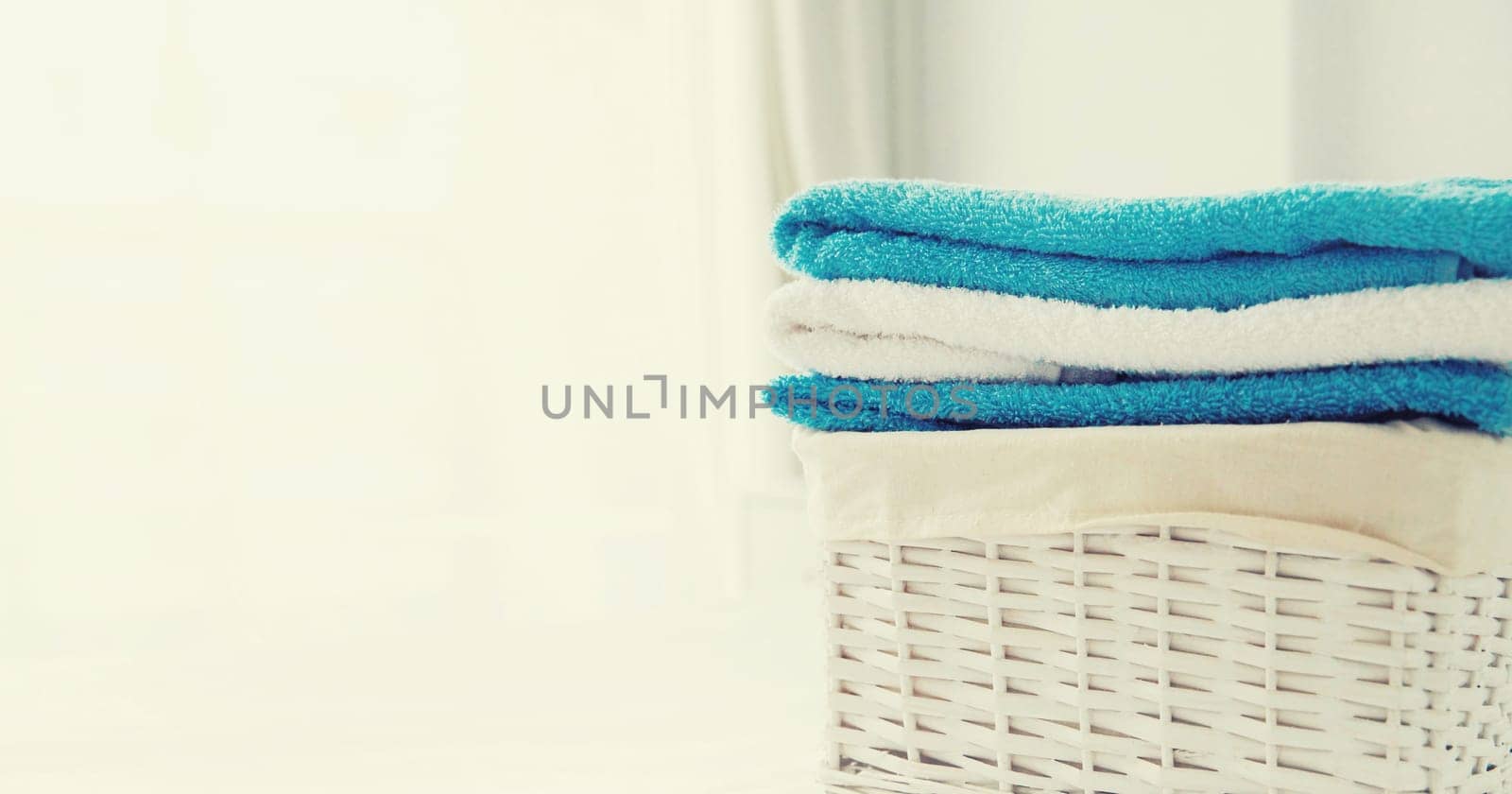 Wicker laundry basket with clean folded towels on the bed by Rohappy