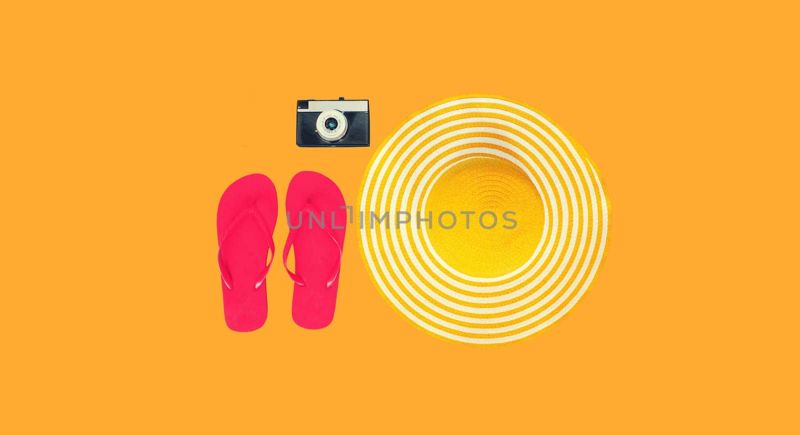 Summer vacation accessories, straw beach hat with flip flops, film camera on yellow studio background, view from above