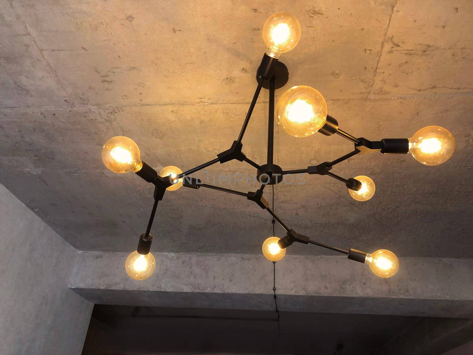 Light bulbs with warm lighting in stylish chandelier with exposed wiring on gray concrete ceiling, interior in retro loft design